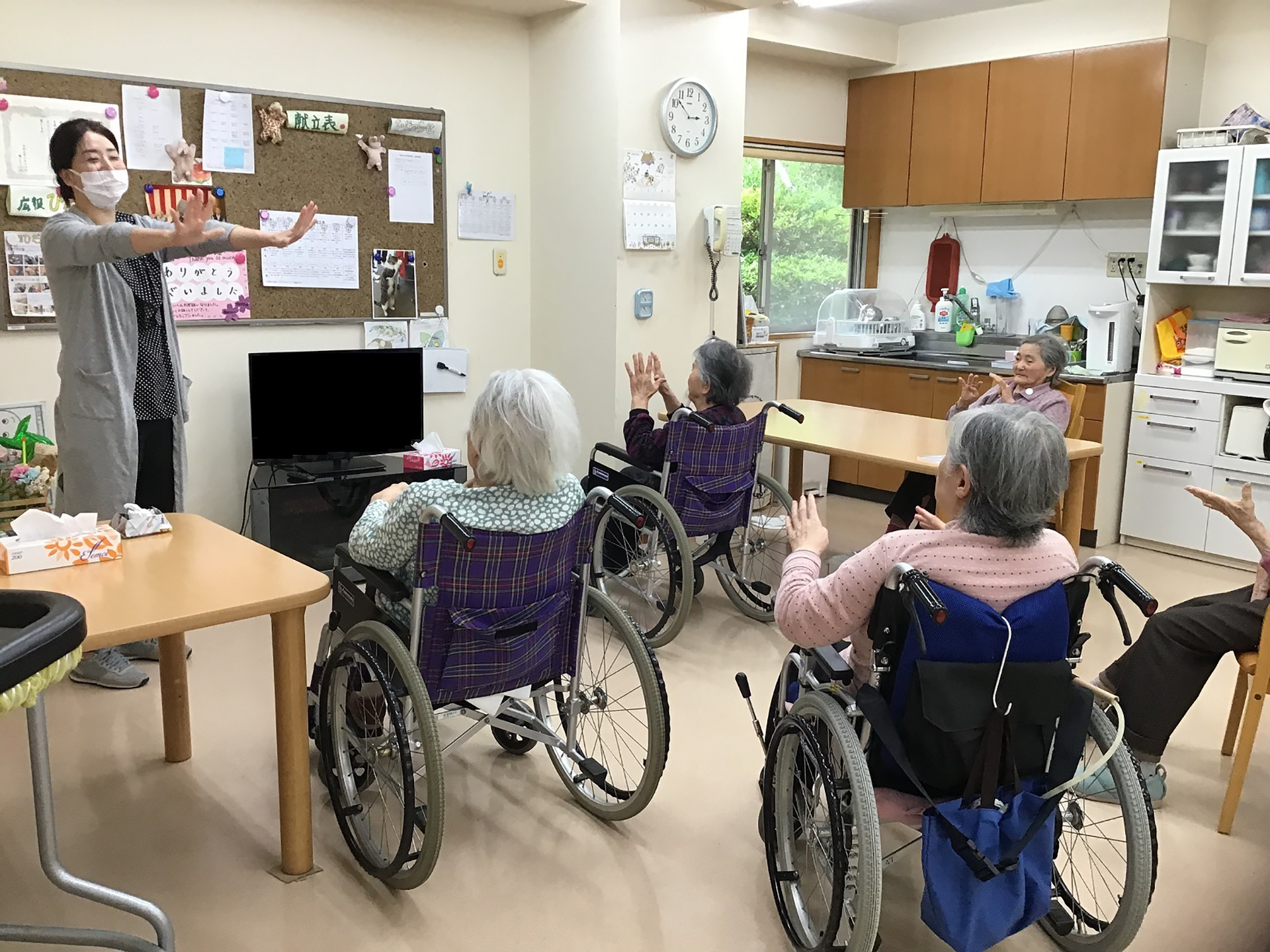 介護施設でのレクリエーション活動。スタッフが車椅子の入居者たちと体操をしている様子。